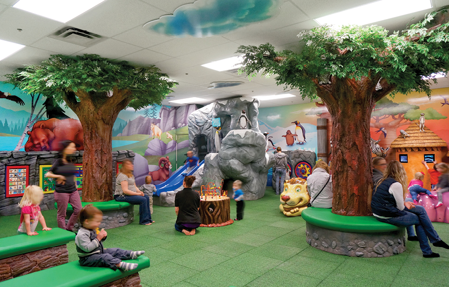A mall kids play area with sculpted trees, play structures, and wall mural modeled off of the local zoo