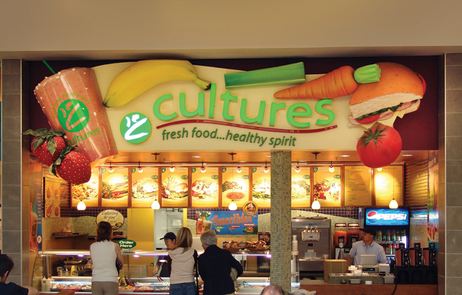 Food court vendor signage with giant sculpted fruits and vegetables